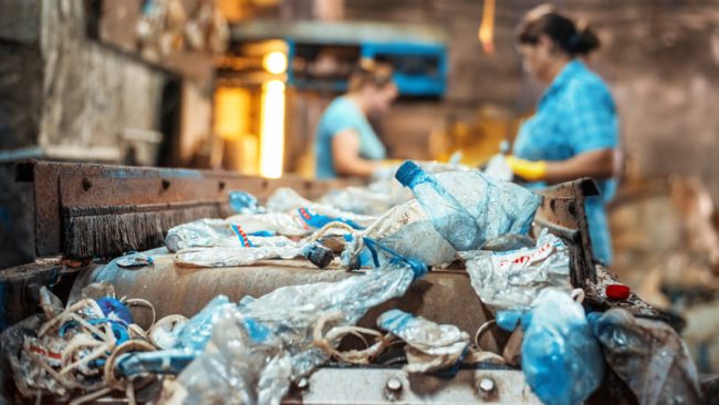 basura-plastica-en-una-cinta-transportadora-en-la-fabrica-de-reciclaje-de-residuos-trabajadores-en-el-fondo (1) (1) Prácticas sostenibles: Clave para preservar nuestros ecosistemas.