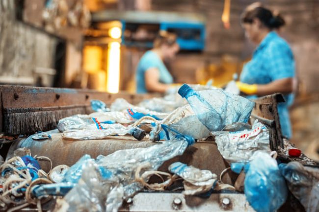 basura-plastica-en-una-cinta-transportadora-en-la-fabrica-de-reciclaje-de-residuos-trabajadores-en-el-fondo (1) (1) Prácticas sostenibles: Clave para preservar nuestros ecosistemas.