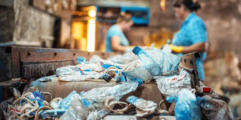 basura-plastica-en-una-cinta-transportadora-en-la-fabrica-de-reciclaje-de-residuos-trabajadores-en-el-fondo (1) (1) Prácticas sostenibles: Clave para preservar nuestros ecosistemas.